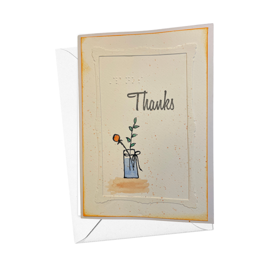 A  greeting card with a white envelope, featuring a hand-drawn illustration of a small  vase  with water and a single orange flower and the word 'Thanks' in script and braille 