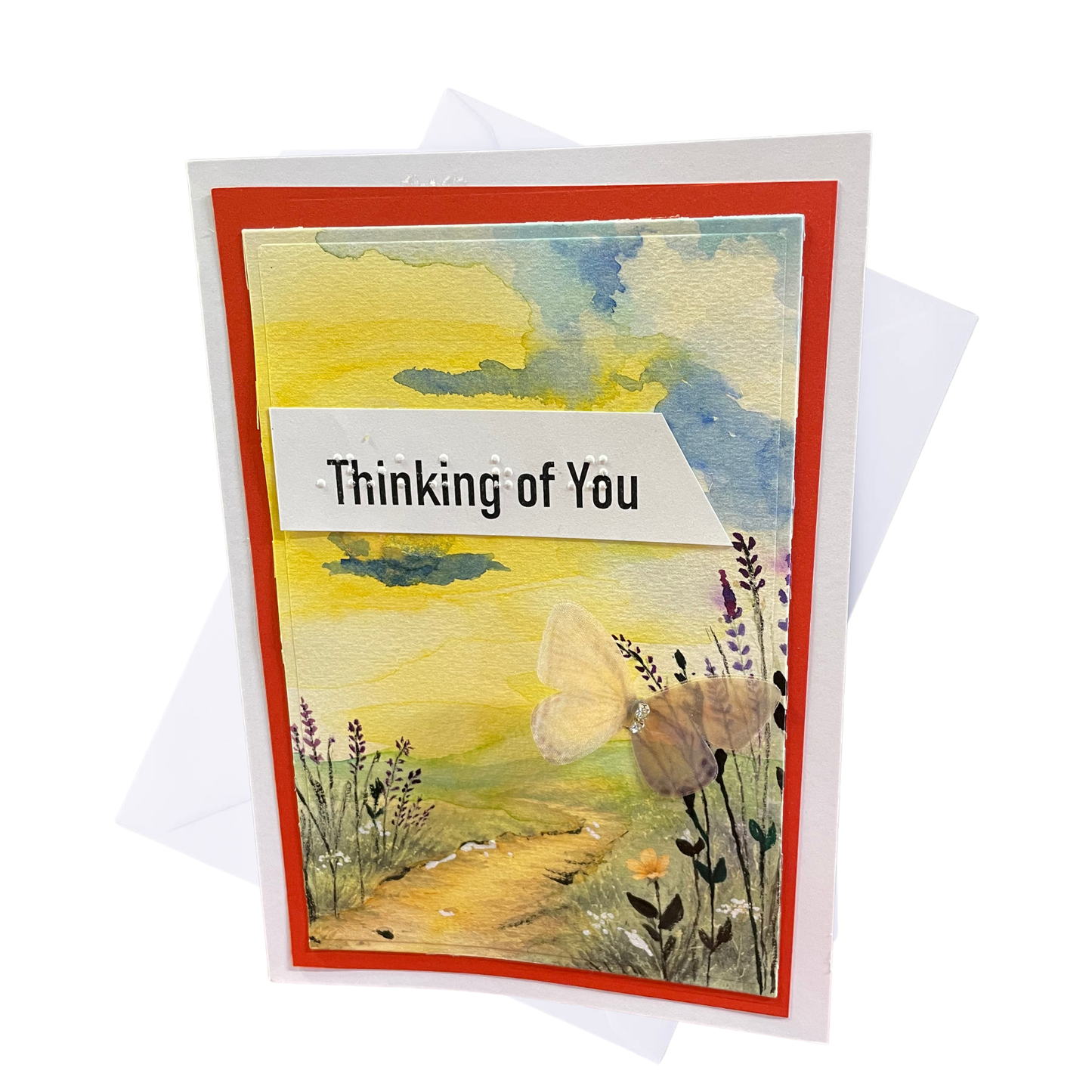 A handmade greeting card with a red border and a watercolor landscape illustration featuring a butterfly, a path, and wildflowers. The card reads 'Thinking of You' in braille and print on a white banner.