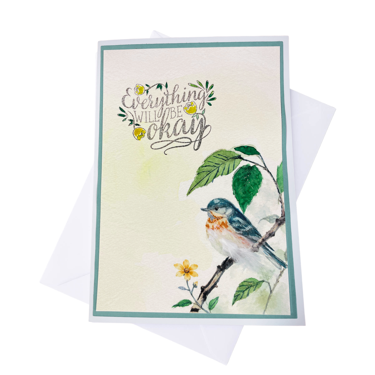  A greeting card with a watercolor bird on a branch with tactile feather and the phrase 'Everything will be okay' in script, shown with a white envelope behind it on a white background.
