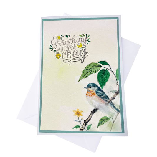  A greeting card with a watercolor bird on a branch with tactile feather and the phrase 'Everything will be okay' in script, shown with a white envelope behind it on a white background.